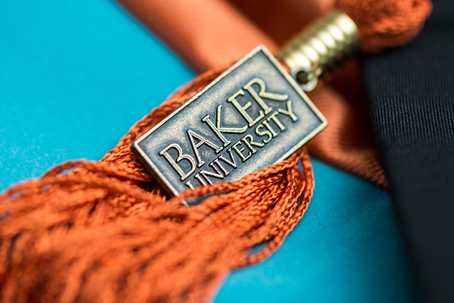 Orange graduation cap tassel with a Baker University metal tag.