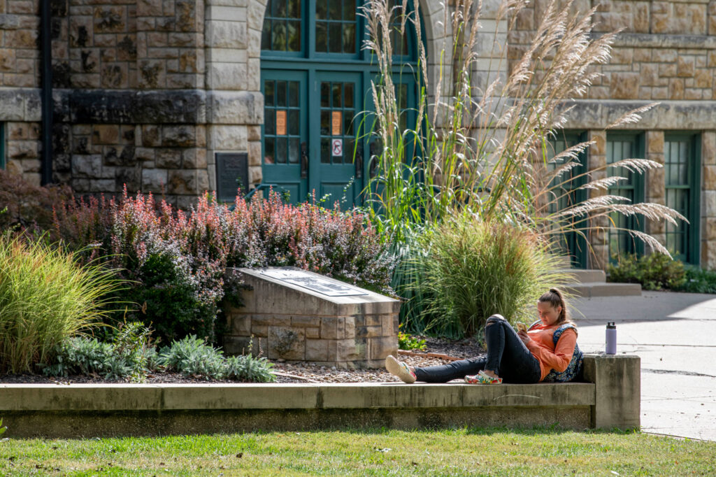 Student on campus relaxing in front of Mabee Hall.