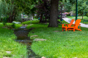 Baldwin City campus. orange Adirondack chairs next to the creek in summer