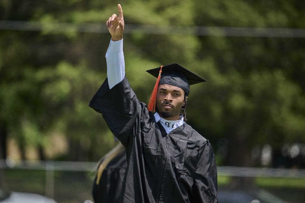 Baker University grad pointing to sky during commencement ceremony